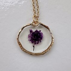 a purple flower in a glass pendant on a gold chain