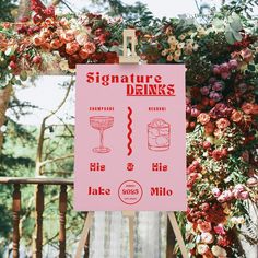 a pink sign hanging from the side of a wooden fence next to flowers and greenery