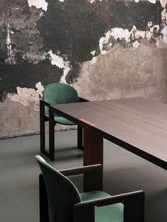 an empty table and two chairs in front of a wall with peeling paint on it