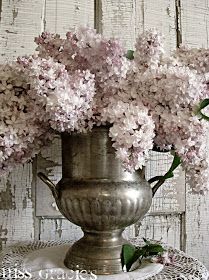 a silver vase filled with pink flowers on top of a white doily covered table