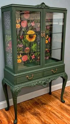 a green china cabinet with flowers painted on the front and sides, sitting on a hard wood floor