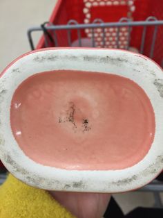 a person holding up a pink and white bowl in front of a red shopping cart