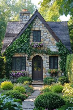 a small stone house with lots of greenery on the front and side windows, surrounded by bushes and flowers