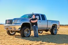 a man standing next to a silver truck on top of a dry grass covered field