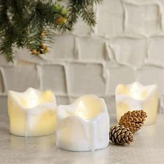 three lit candles sitting on top of a counter next to pine cones and evergreen branches