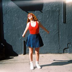 a woman in a red top and blue skirt is standing on the sidewalk with her arms outstretched