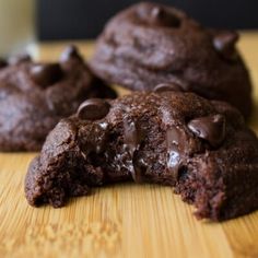 three chocolate cookies on a cutting board with a glass of milk in the background and one half eaten