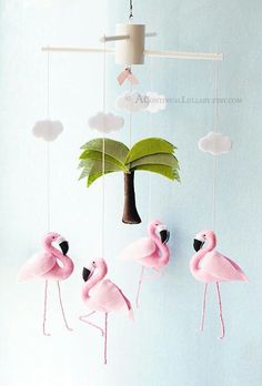 three pink flamingos are hanging from a string with a palm tree in the background