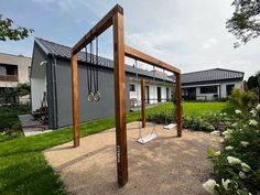 an outdoor playground with swings and plants in front of a house on a sunny day