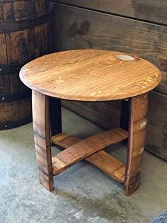 a round wooden table sitting next to two barrels on the floor in front of a wall