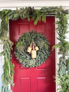 a red front door decorated with evergreen wreaths and bells for the christmas holiday season