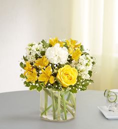 a vase filled with yellow and white flowers sitting on top of a table next to a pair of glasses