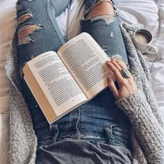 a person laying on a bed with an open book and cup of coffee in their lap