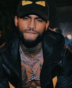 a tattooed man wearing a black hat and jacket with yellow eyes on his face is looking at the camera