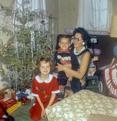 a woman and two children are sitting in front of a christmas tree