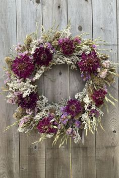 a wreath made out of dried flowers on a wooden fence with purple and white colors