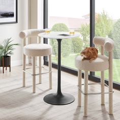 a cat sitting on a chair in front of a table with two stools next to it