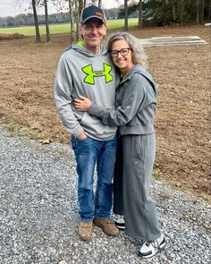 a man and woman standing next to each other in front of a field with trees