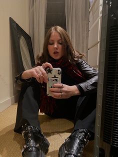 a woman sitting on the floor taking a selfie with her cell phone while wearing black boots