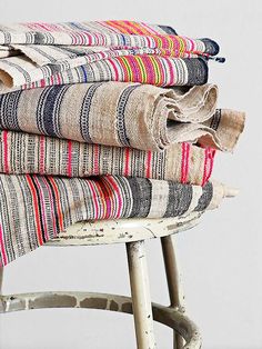 a stack of folded towels sitting on top of a wooden stool next to a white wall