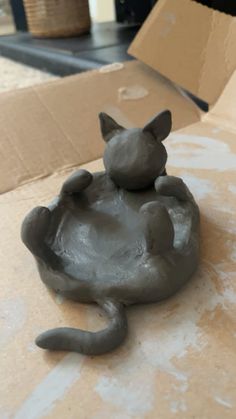 a clay cat sitting on top of a cardboard box with it's tail curled up