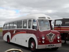 an old red and white bus is parked in a parking lot next to other buses