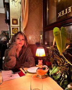 a woman sitting at a table in front of a lamp