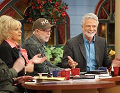 three people sitting at a table talking to each other on the set of an old tv show