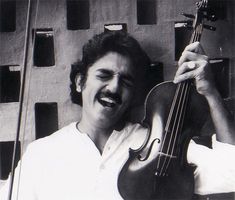 a man holding a violin in his right hand and smiling while standing next to a microphone