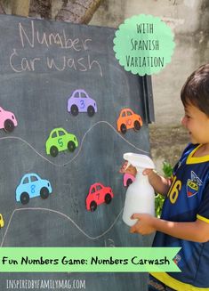 a young boy holding a spray bottle next to a chalk board with cars drawn on it