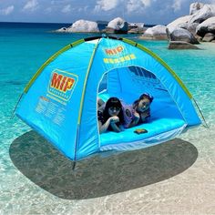 two children laying in a blue tent on the beach