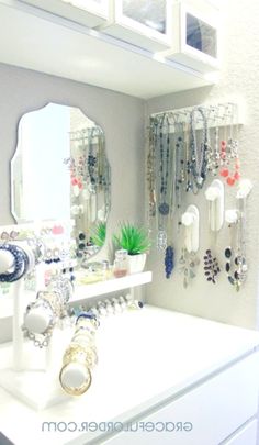 a white table topped with lots of jewelry next to a mirror and shelf filled with necklaces