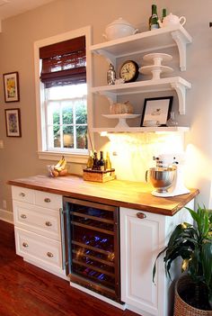 a kitchen with white cabinets and wooden counter tops, an open wine cooler in the center