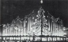 an old black and white photo of a lit christmas tree in front of a building