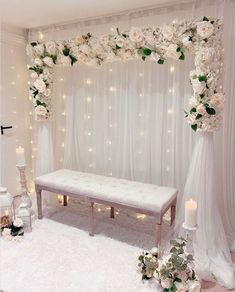 a white wedding ceremony setup with flowers and lights on the wall, bench for seating