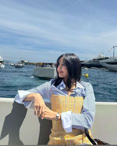 a woman sitting on a wall next to the ocean with boats in the water behind her