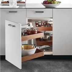 an open cabinet in a kitchen filled with pots and pans next to a bowl of fruit