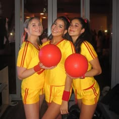 three girls in yellow and red soccer uniforms holding large balls with their arms around each other