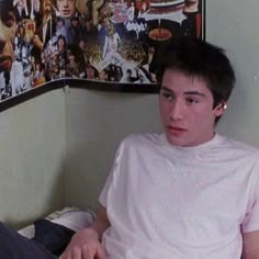 a young man sitting on top of a bed in front of a wall with posters