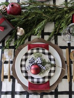 a place setting with christmas decorations and silverware on a black and white checkered table cloth