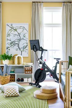 a room with yellow walls, green and white striped curtains, an exercise bike in the foreground