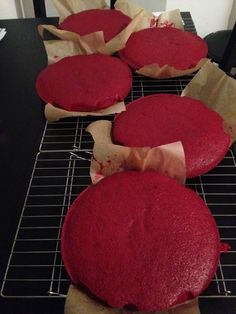 four red cakes sitting on top of a cooling rack next to brown paper bag bags