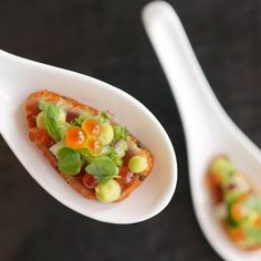 two spoons with food on them sitting next to each other in front of a black surface