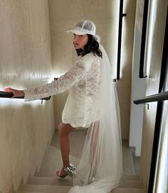 a woman in a white dress and hat is walking down the stairs