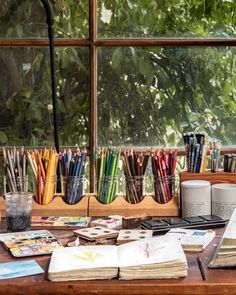 an open book sitting on top of a wooden table next to a cup filled with colored pencils