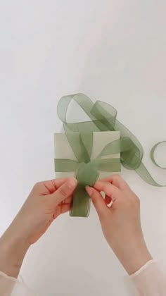 two hands holding a green gift box with a ribbon on it and another hand reaching for the bow