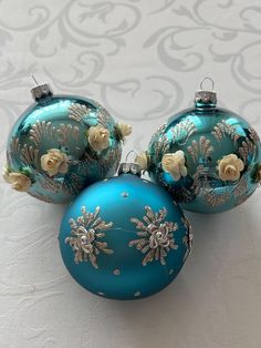 two blue christmas ornaments with white roses on them sitting on a tablecloth covered surface