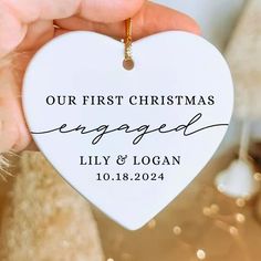 a person holding a heart shaped ornament with the words our first christmas engaged