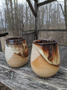 two brown and white cups sitting on top of a wooden table next to each other