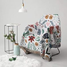 a chair with a blanket on it next to a table and vase filled with flowers